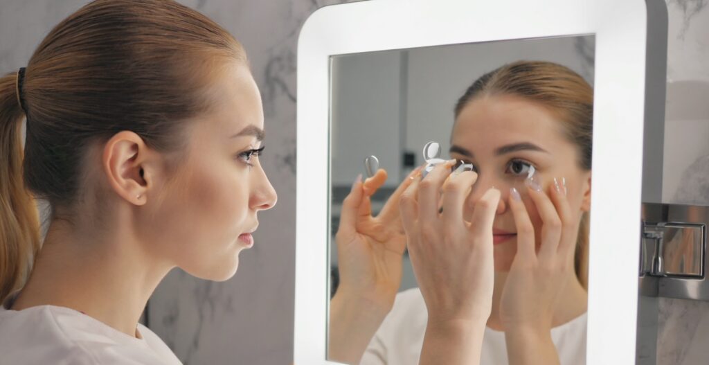 Woman inserting scleral contact lens in front of mirror